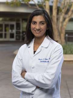 Monica Khitri in a white lab coat standing confidently with her arms crossed and smiling outdoors