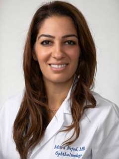 Headshot Dr. Mitra Nejad with long brown hair wearing a lab coat and smilling