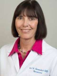 Headshot of Dr. Gail Greendale, a woman with shoulder-length brown hair and bangs, smiling while wearing a white lab coat over a pink shirt.