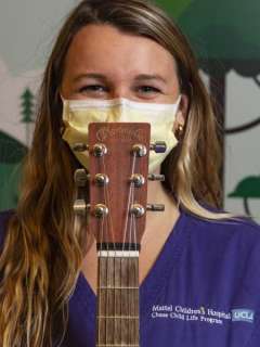 A headshot of music therapist Jenna Bollard, smiling with her eyes and holding a guitar.