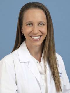 Stacy Pineles wearing a white lab coat against a blue background.