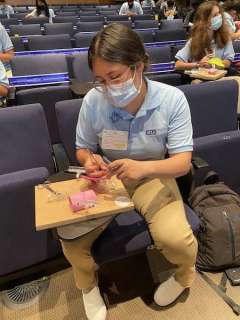 Student in a blue polo shirt working on a project with materials in a classroom setting.