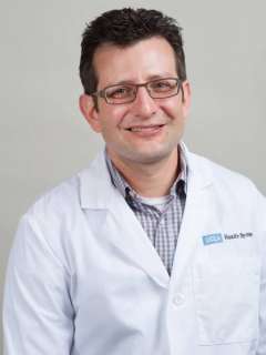 Professional in a lab coat, posed against a neutral background.