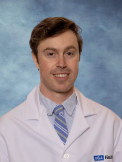 headshot of Dr. Nicholas Kraus in a white lab coat in front of a blue background