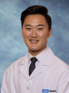A headshot of Dr. Andy Moon smiling and wearing a white lab coat with a dark tie.