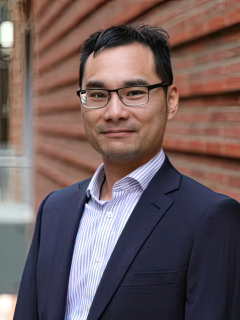Dr. Neil Lin wearing a dark blue suit and standing against brick wall