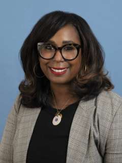Dr. Eraka Bath wearing a blazer and necklace, with a blue background.