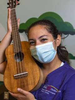A headshot of music therapist Bethany Pincus smiling with her eyes. She is holding a ukulele.