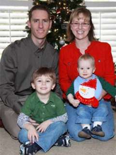 Parents with a young boy and baby seated in front of a Christmas tree