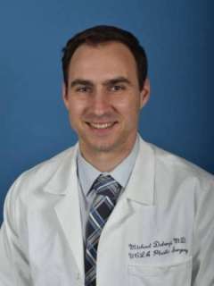 Dr. Michael DeLong with a pleasant, professional demeanor smiles at the camera, wearing a white lab coat and a striped tie.