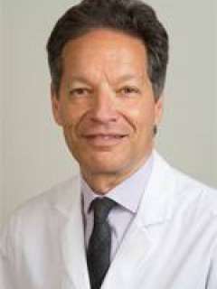 A professional headshot of Dr. Ira Kurtz, a man with wavy hair, smiling in a white lab coat with a tie against a light background.