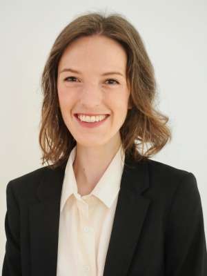 A woman with brown hair, wearing a suit jacket with a white shirt
