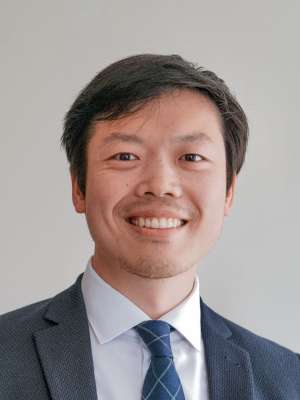 Smiling person wearing a suit and tie against a neutral light background