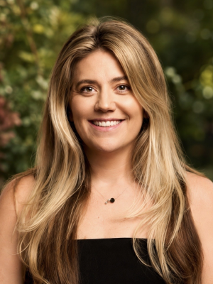 Smiling woman with long blonde hair against a blurred leafy background