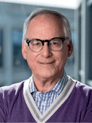 Steven Fink in a purple sweater with a plaid shirt standing indoors.