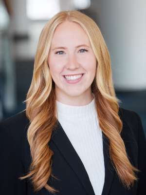 A woman with blonde hair, wearing a white sweater with a suit jacket