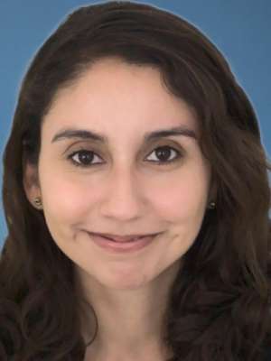 Smiling woman headshot with long dark hair on blue background.
