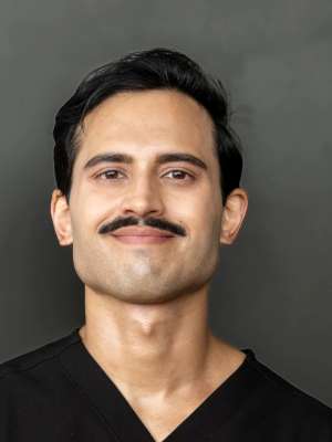 Head-and-shoulders portrait of man with mustache wearing dark scrub top on gray background