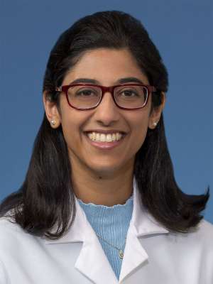 Smiling person in white lab coat and red glasses on blue background.