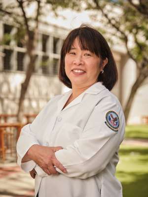 Dr. Cathy Lee, standing with arms crossed, smiling outside.