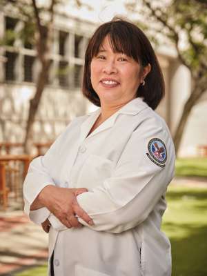 Dr. Cathy Lee, standing with arms crossed, smiling outside.