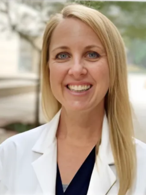 Smiling woman in a white lab coat with long blonde hair.