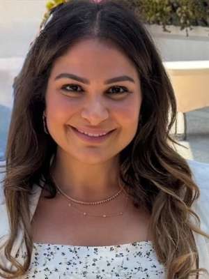 Woman with long hair wearing a white dress and layering jewelry outdoors.