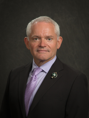 Dan Milner, MD in a black suit and purple tie with dark background