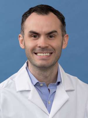 White coat head shot of Daniel Hawkins, smiling at the camera