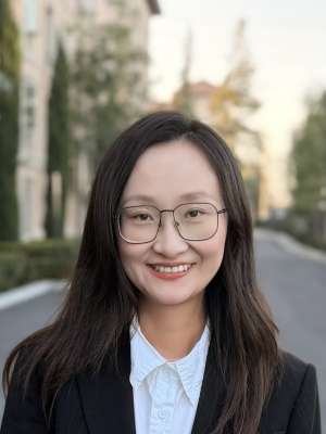 Professional headshot of smiling woman with glasses in blazer outdoors