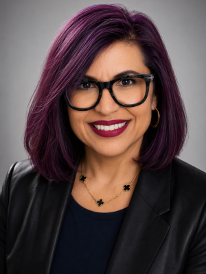 DeeAnna Serna smiling with purple hair, black glasses, and black blazer