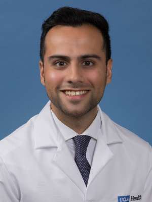 Head shot of Adnan Husein in white lab coat, smiling at camera