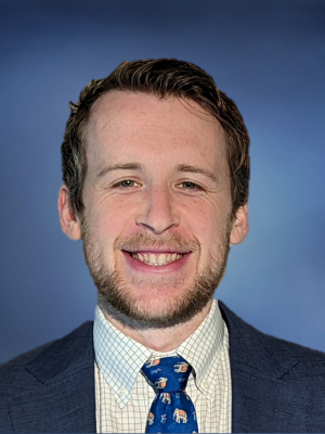Head shot of Jacob Klickstein in a suit, smiling at the camera