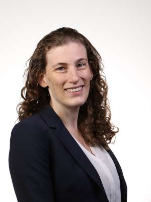 Smiling woman with curly hair wearing navy blazer and white blouse.