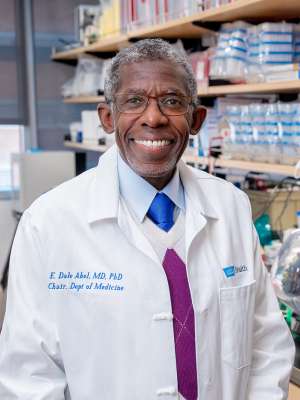 Doctor Abel in a white lab coat standing in a laboratory with equipment and shelves in the background