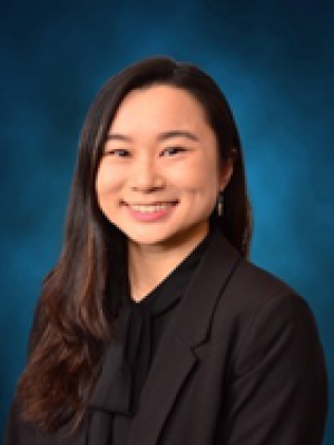Headshot with blurred face, person in black blazer against blue backdrop