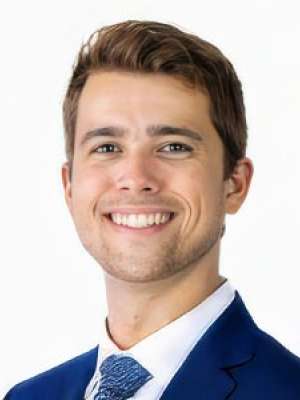 Ryan Miller smiling headshot in blue suit and tie on white background