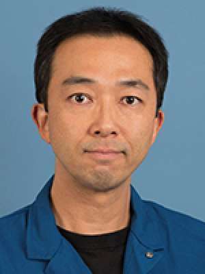 Head-and-shoulders portrait of a man wearing a blue jacket against a blue background.