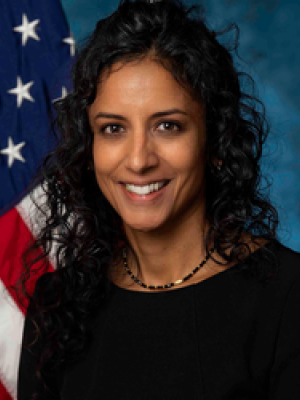 headshot of Dr. Anjani Reddy in black blouse with flag in the background