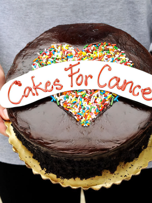 Cakes for Cancer founder Abigail Nathanon holding a chocolate cake, with "Cakes for cancer" written on top