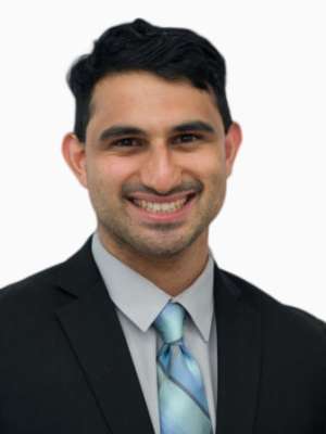 Madhav Nekkar smiling headshot wearing dark suit and blue striped tie