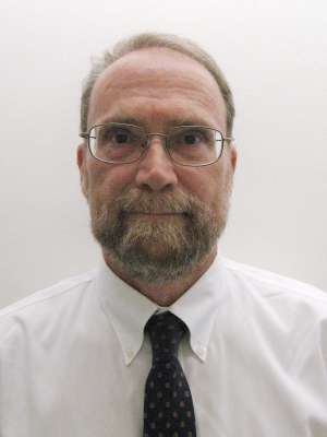 Person wearing white dress shirt and dark patterned tie against plain white wall