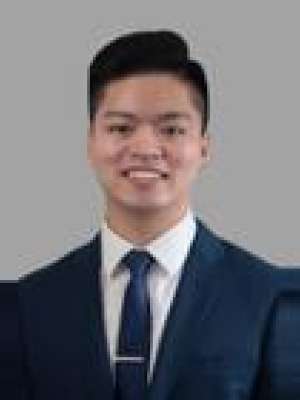 person wearing navy suit and tie against gray background.