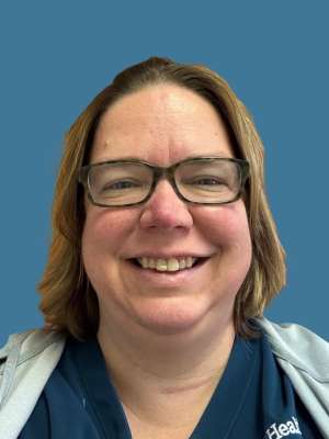 A person wearing a navy blue shirt with a gray cardigan against a blue background.