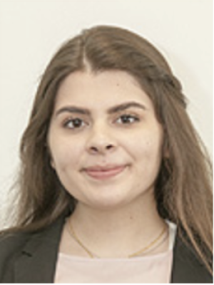 Headshot of a person with long brown hair, wearing a blazer and pink top.