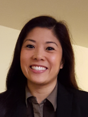Hanh Tan with long dark hair wearing a dark blazer and brown shirt, smiling indoors.