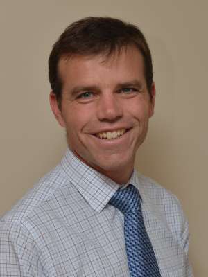 Smiling man headshot in collared shirt and blue tie on beige background