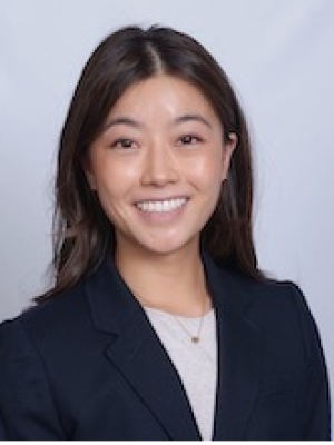 Headshot of a woman wearing a dark blazer and necklace on a light background.