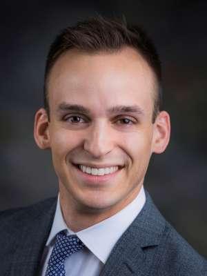 Smiling man in suit and tie against dark studio background.