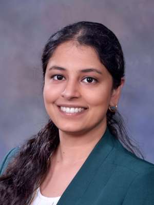 Smiling professional woman wearing green blazer against soft gray-blue backdrop.